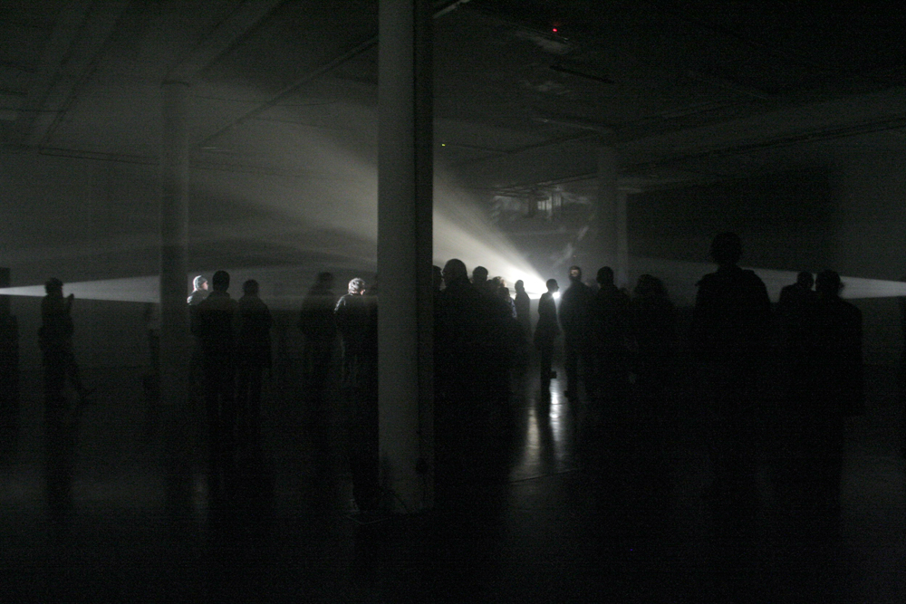 An audience milling about among beams of light