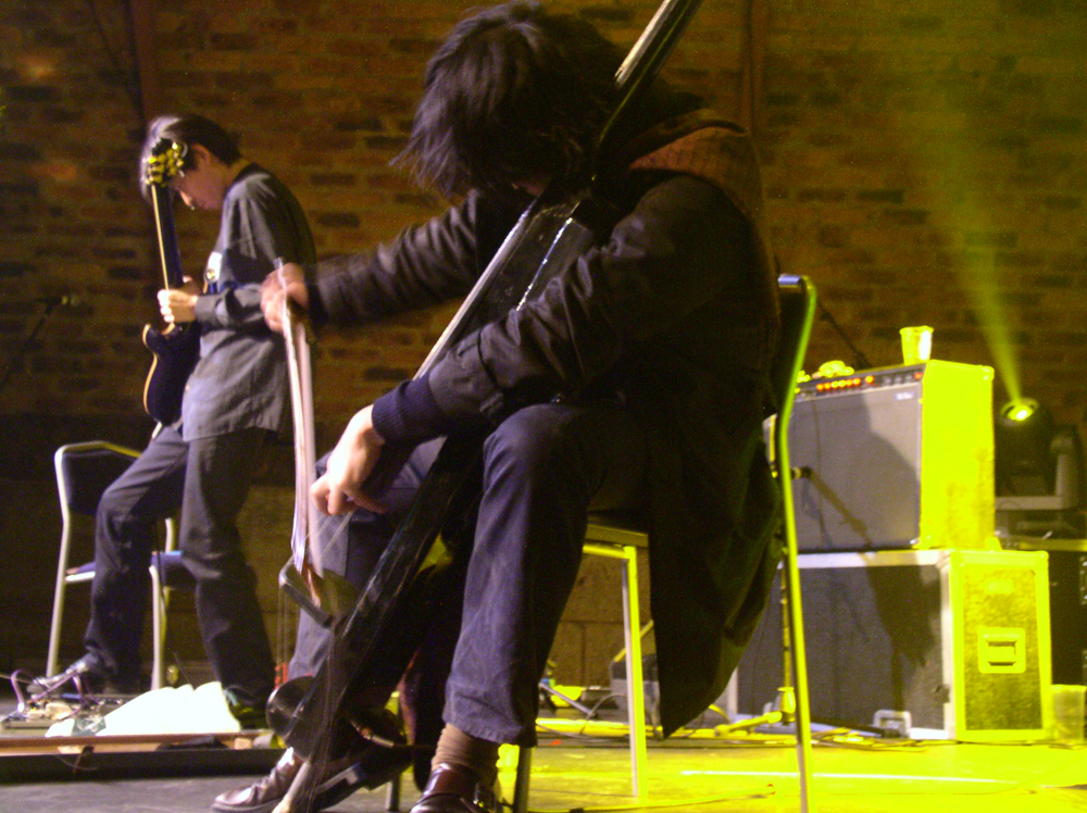 Exias J playing guitars and double bass on stage at INSTAL 04