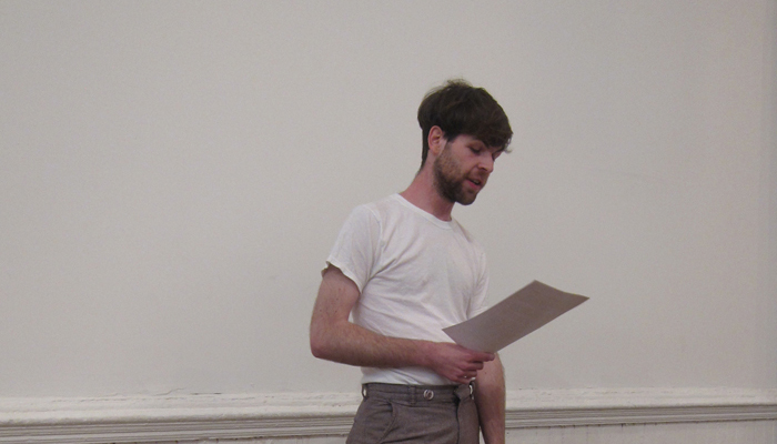 Jordan Lord standing reading from a paper in a white room