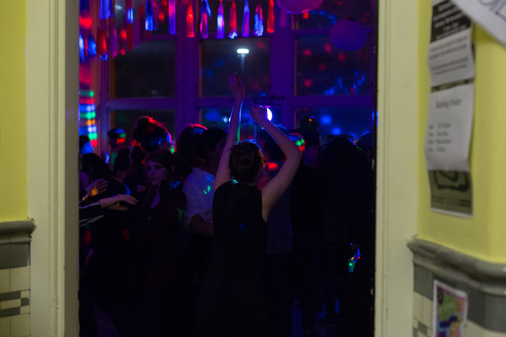 Through a door there is a party with disco lights and dancing