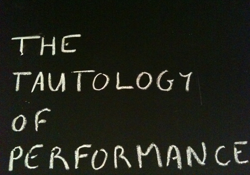 "The Tautology of Performance" written on a board in chalk