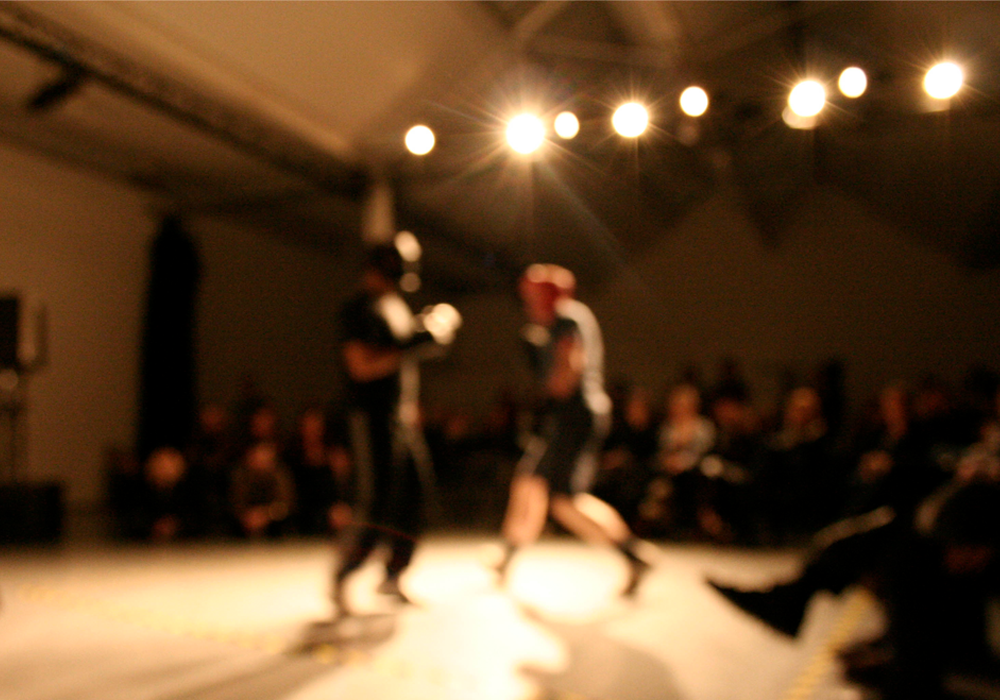 Two figures boxing in front of an audience