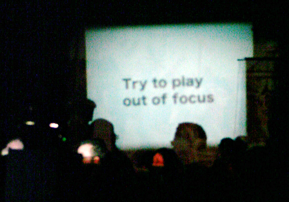 A blurry projection screen has the words "Try to play out of focus"