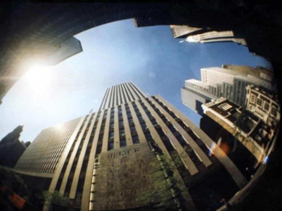 a fisheye lens looks up a blue sky with skyscrapers towering around
