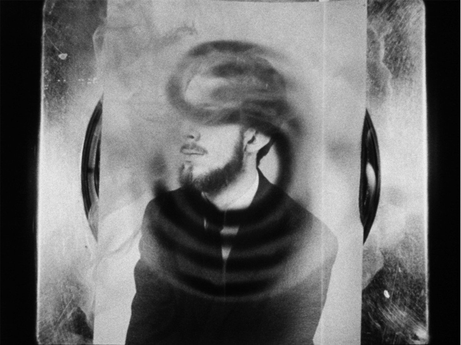 A black and while still of a photograph of a man melting on a stove