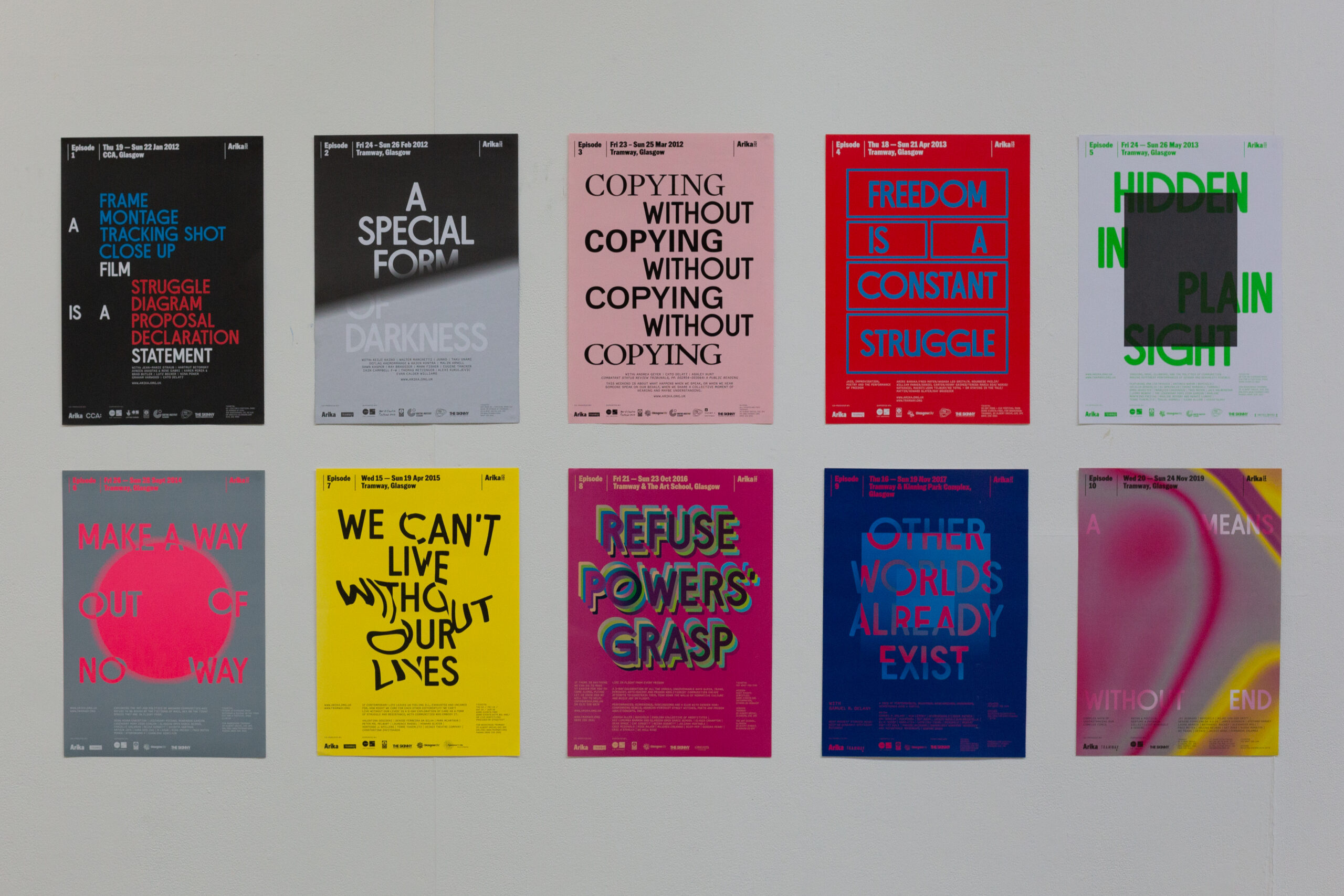 each of Arika's Episode posters arranged in order, from Episode 1 to Episode 10, a brightly coloured arrangement of shapes and text on a white wall.