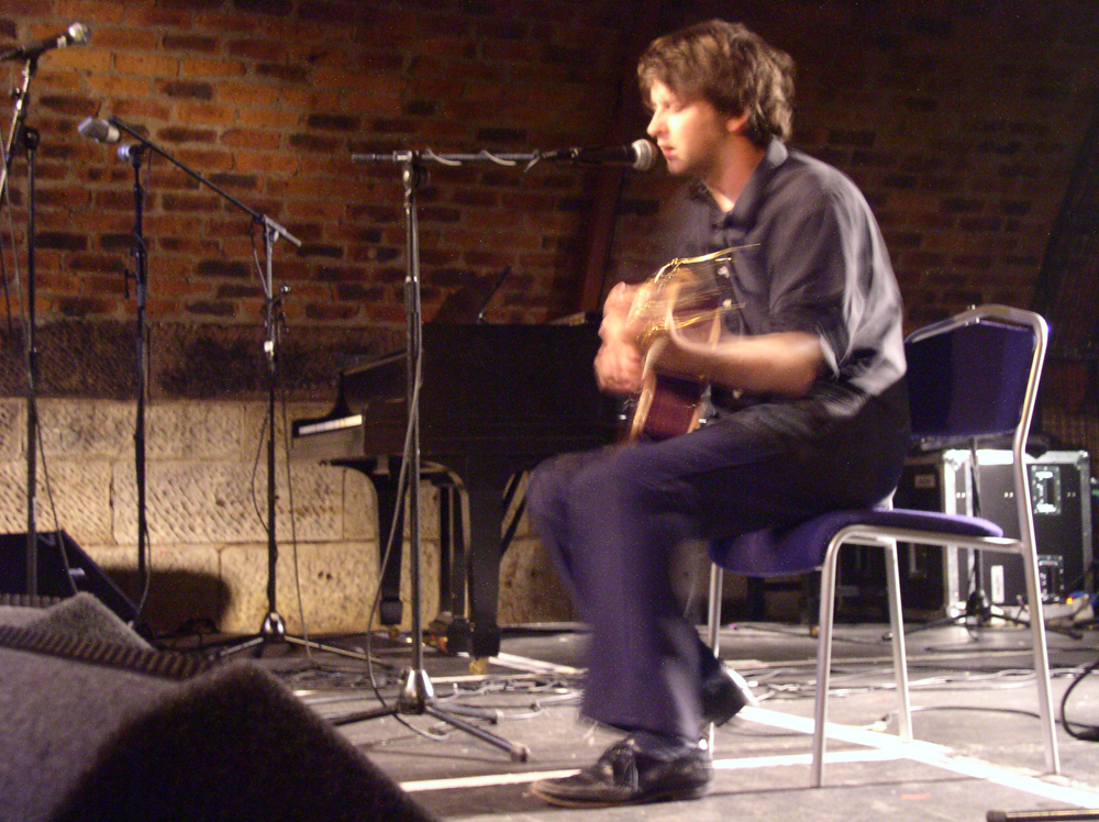 A seated Ben Chasney plays guitar on a brightly illuminated stage