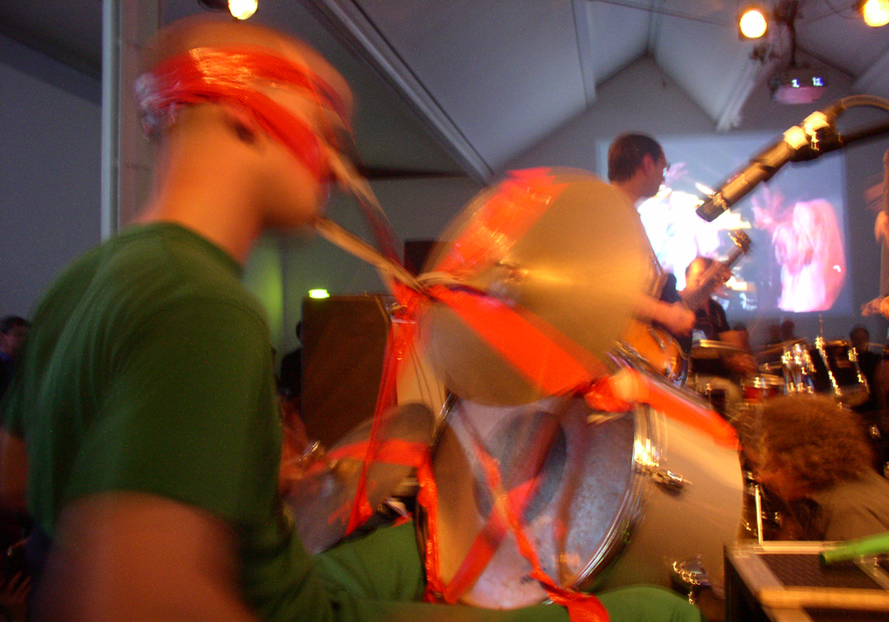 a man in green clothes is wrapped to a drum kit by red tape