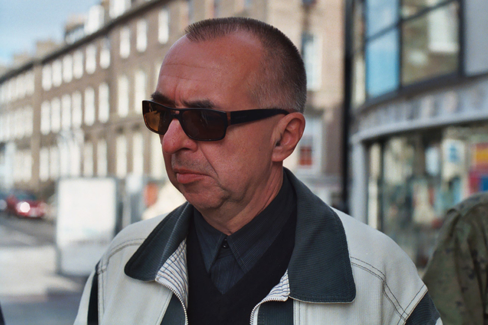 A man in sunglasses standing in front of a sunny row of tenements 