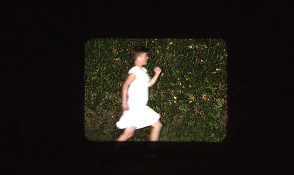 A woman in a white dress jogs across a frame screened on a wall