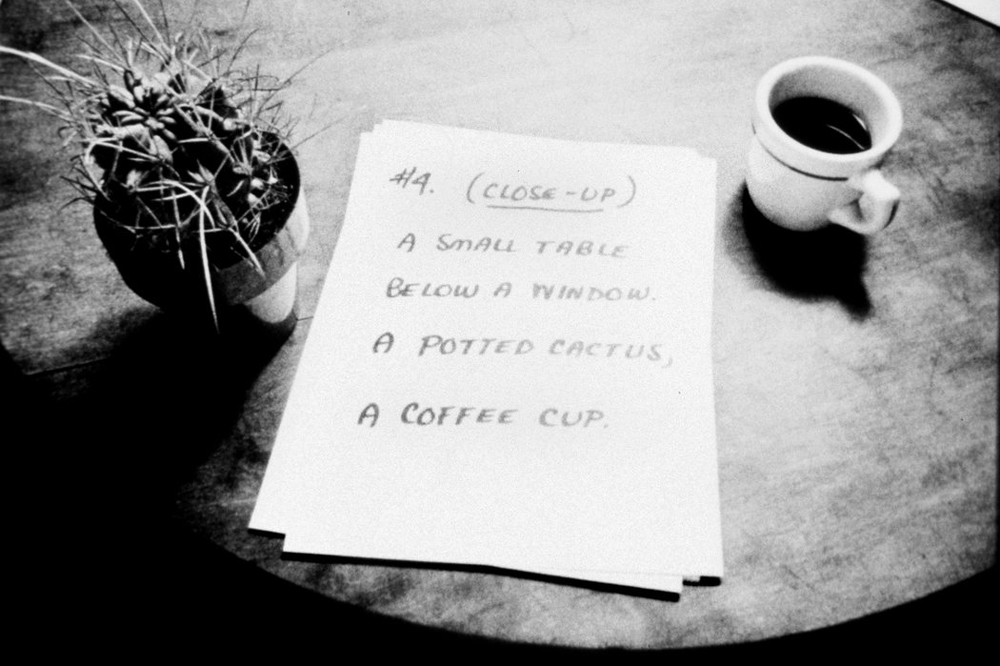 A cactus and coffee cup and a sheet of paper sit on a table
