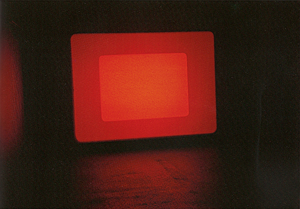 at the end of a dark gallery a screen throbs with layers rectangles of red