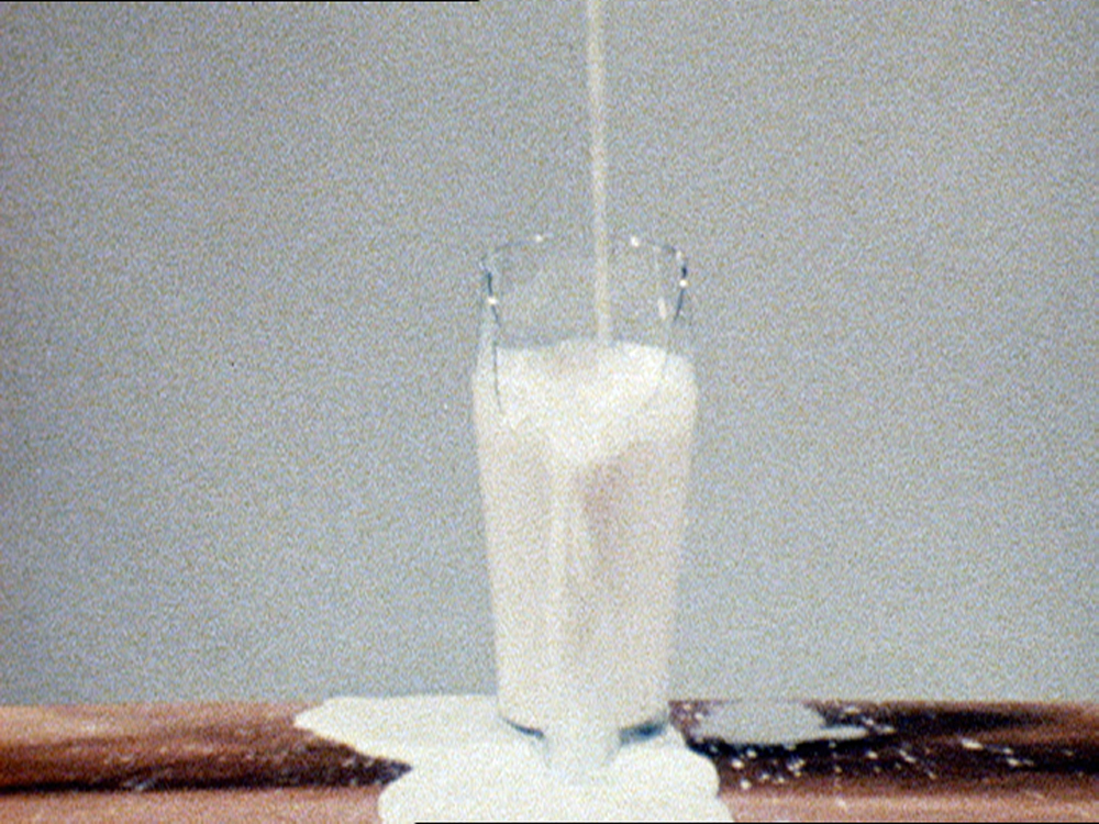 A glass spilling over with milk sat on a table