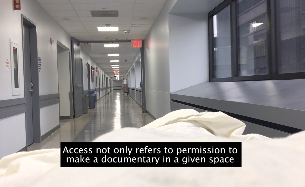 A film still shows an interior view along a hospital corridor