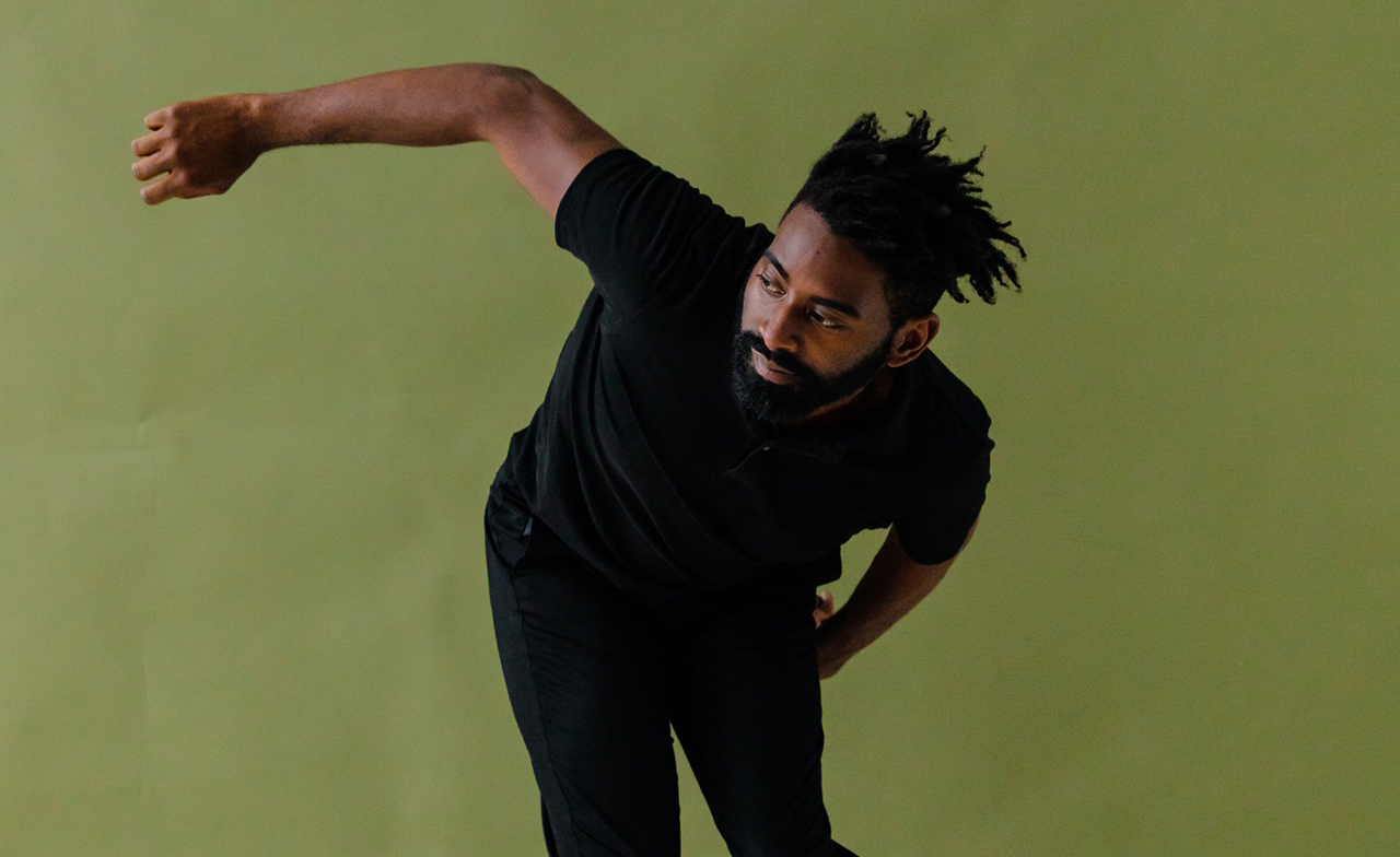 Jerron crouches to one side, right arm extended, infront of a green background