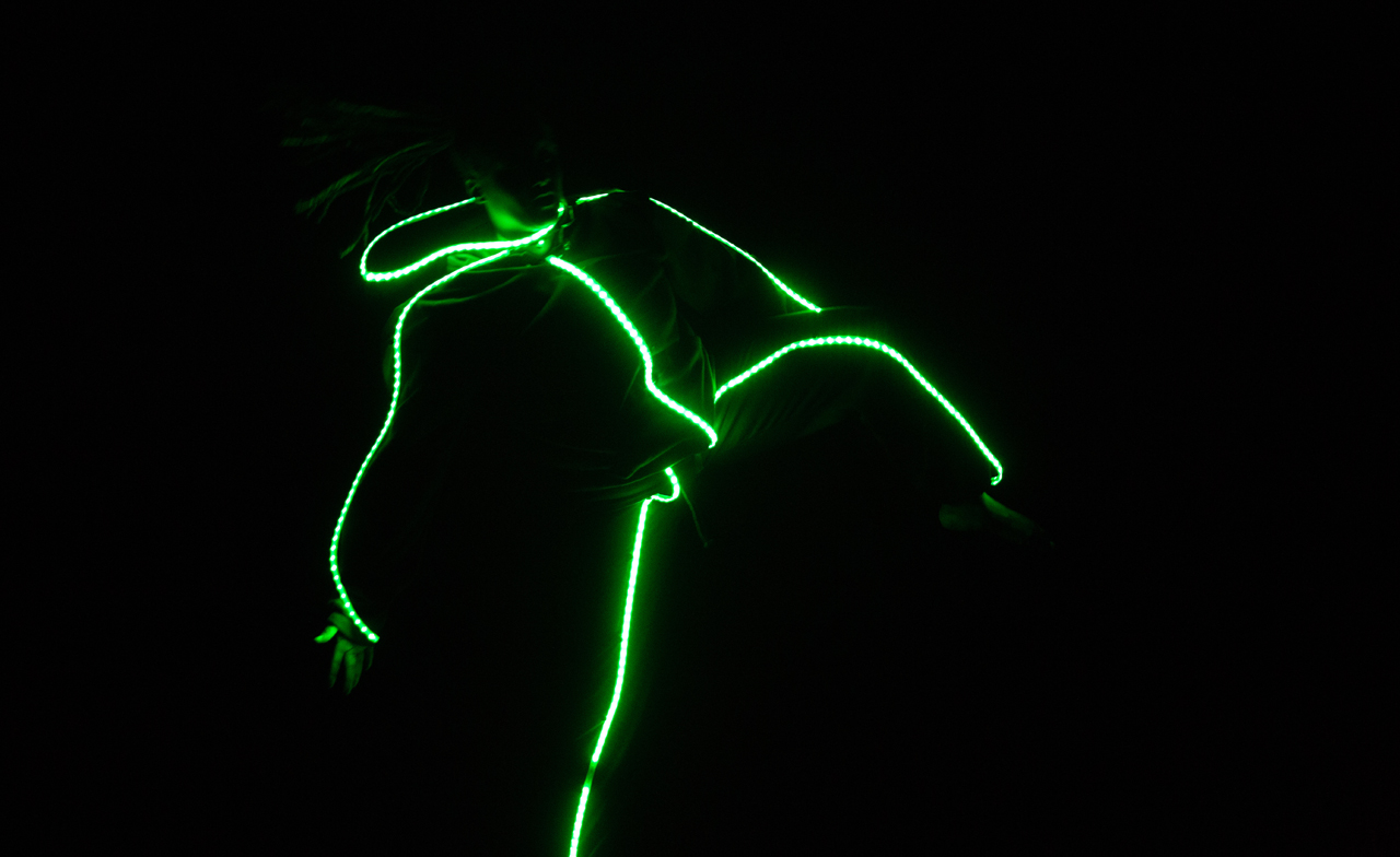 In near darkness, a dancers outline is illuminated by acid green LED rope lighti