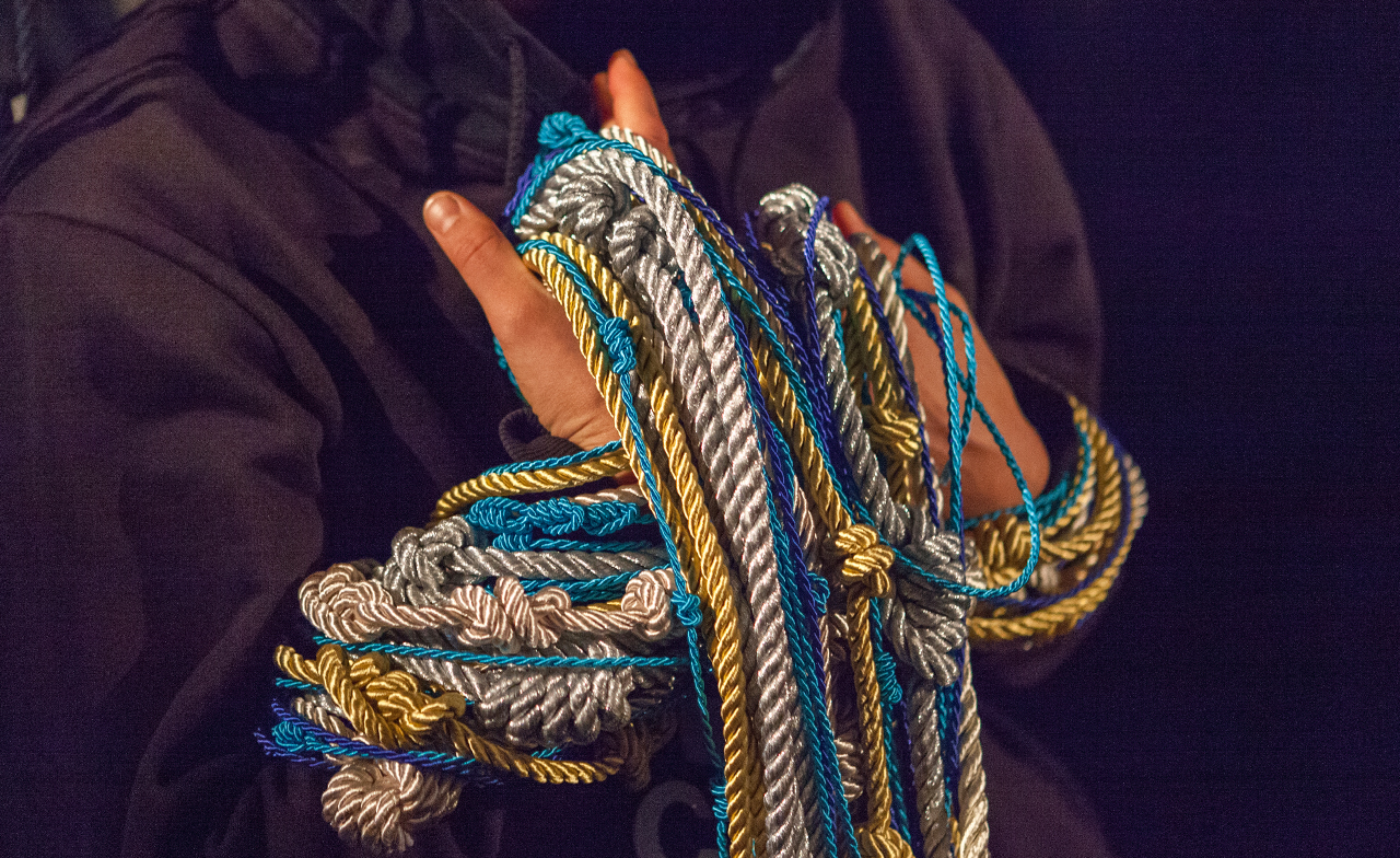 Someone hands are bound in maybe 15 different, irregularly knotted ropes