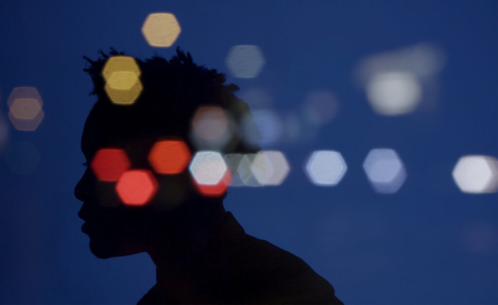Silhouette of a person in front of a blue background overlaid with blurry light