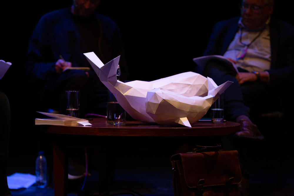 two white whales made of paper perch on a low coffee table