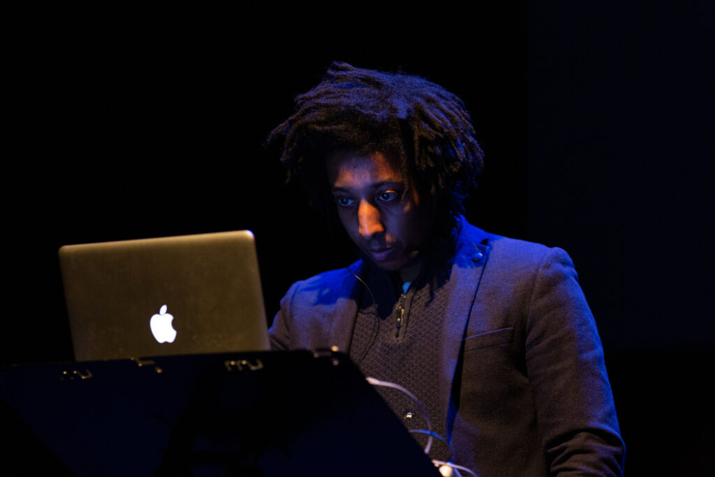 James Goodwin performs in front of a laptop in a dark room