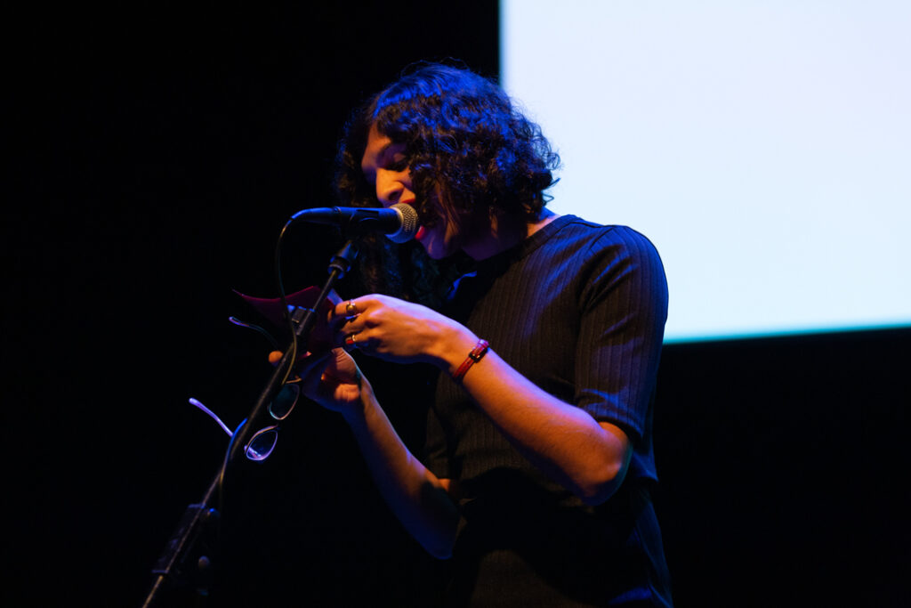 Nat Raha speaks into a microphone while she reads