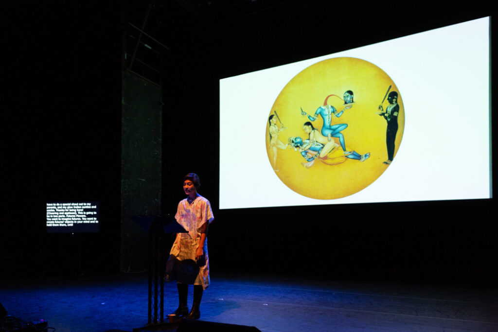 Nisha on stage with glowing screen of a yellow circle with a blue figure drawing