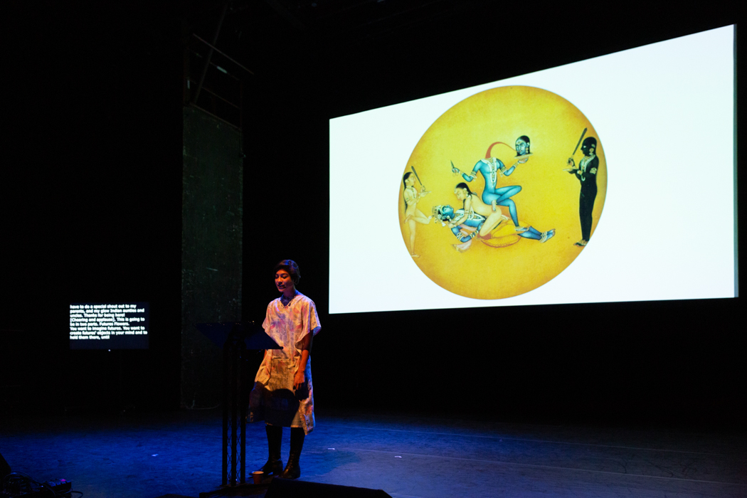 Nisha 在舞台上，屏幕上有黄色圆圈和蓝色图形的发光屏幕