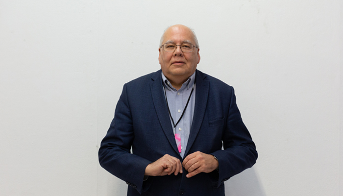 Fernando stands against a white background wearing a blue shirt and suit