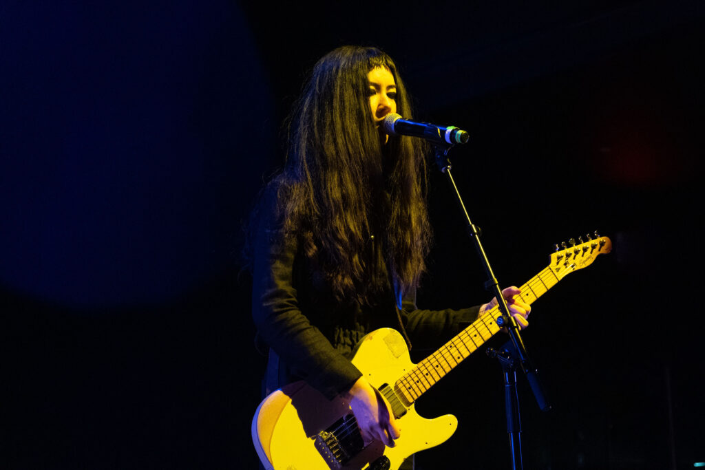 Johanna singing into the mic, holding their cream coloured electric guitar