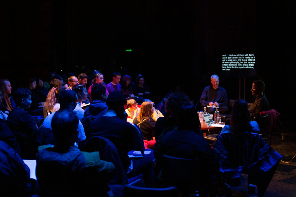 Denise Ferreria da Silva sits on stage whilst delivering a study session to a large audience seated around her