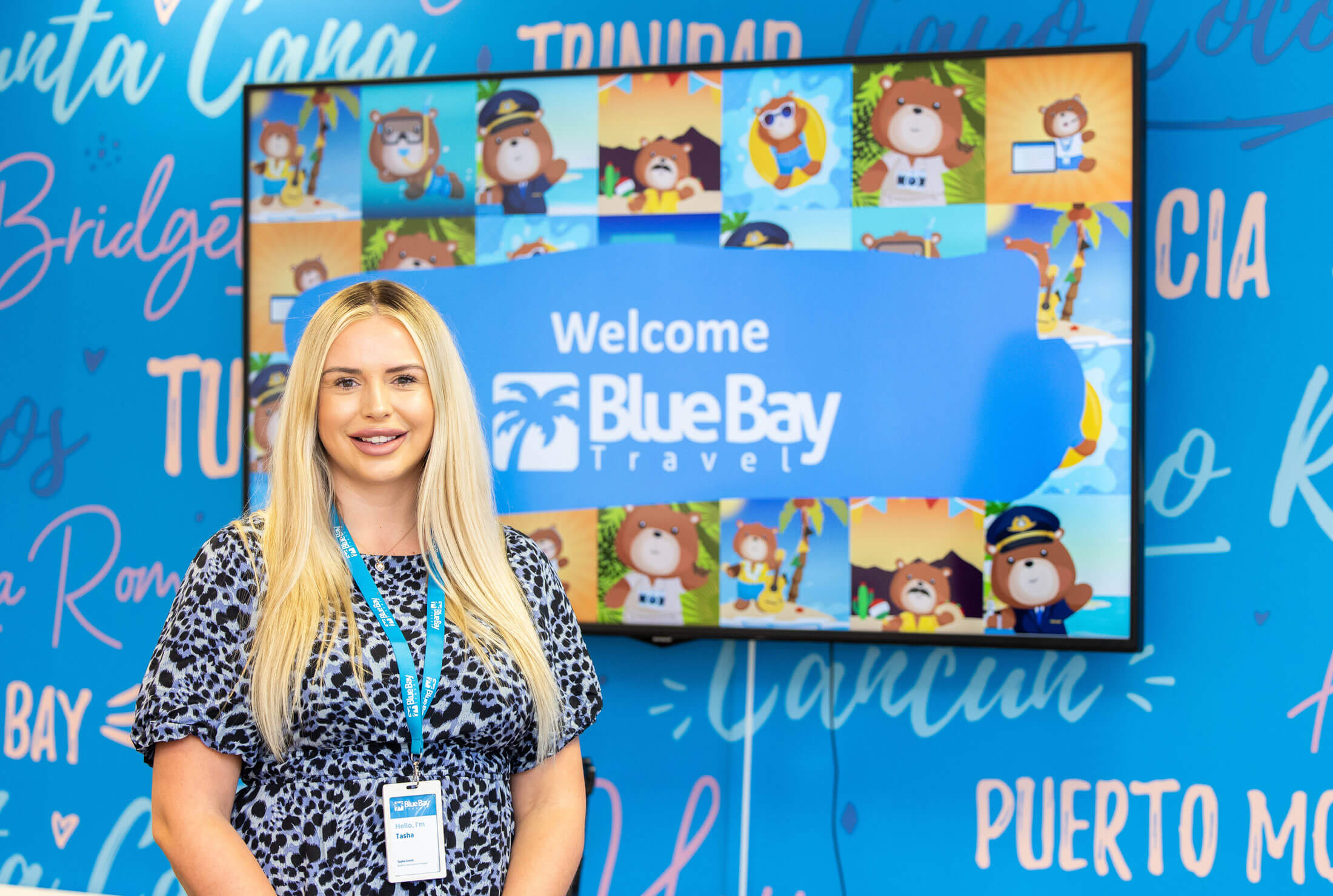 A Business Development Manager in front of a large television screen that says welcome to Blue Bay Travel