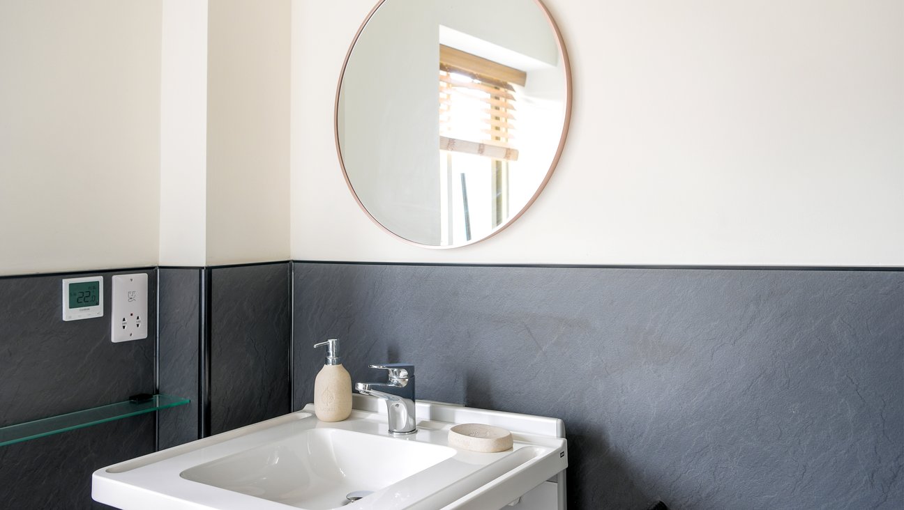 

                                        Adjustable height sink with round mirror and light above, integrated grab rails, shaver socket with shelf below, and towel holder. Also small grey 3 tier trolley to the right hand side
