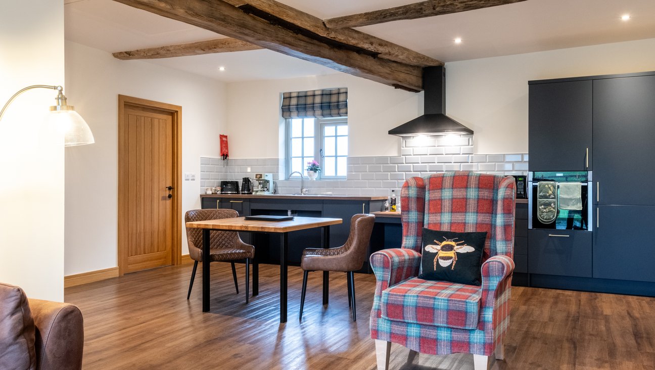 

                                        Wood effect lvt floor with a tartan armchain in foreground. Accessible kitchen in back ground with roll under sink & Hob. Oak kitchen table with Leather chairs, neff hide and slide oven, kettle, microwave, toaster, fridge freezer and expresso machine.