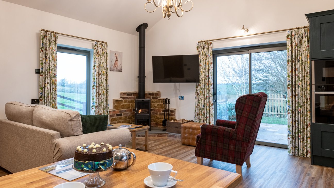 

                                        A table laid for tea in the foreground. a log burning stove in the background, two floor to ceiling windows a large squishy sofa and tartan chair on a non slip oak floor.