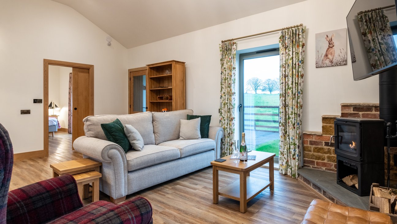 

                                        A tablfront door and book case to the left,  a log burning stove on the right,   floor to ceiling window a large squishy sofa and tartan chair on a non slip oak floor.