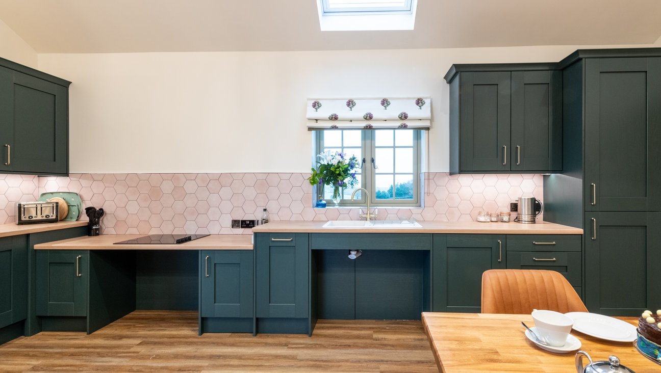 

                                        Roll under sink and hob in green kitchen with pink tiles and clark & clark blind with artichoke flowers on it