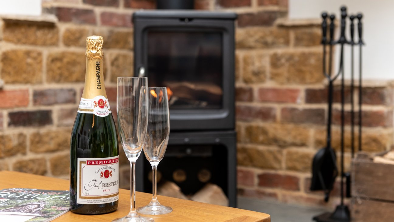 

                                        A Peanut 5 woodburner with a hearth of slate and a combination of ironstone and brick behind it. in the foreground a bottle of champagne and flutes.