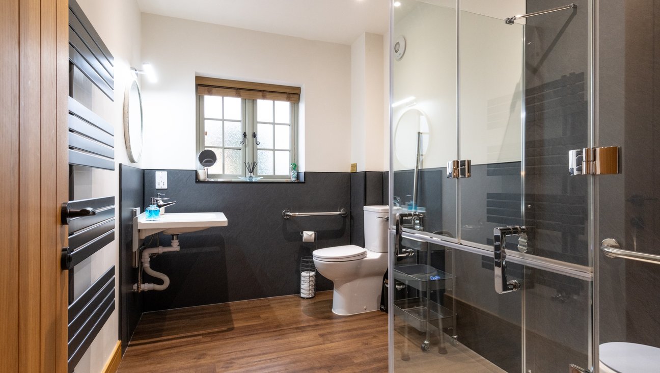 

                                        Bathroom is equipped with a split door AKW shower, hewi adjustable sink with integrated grab bars, and a comfort height toilet on a non slip floor.