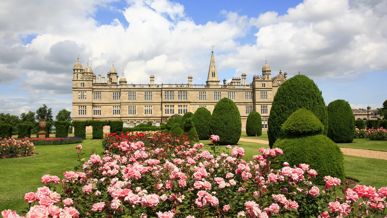 

                                        Pink roses in foreground. behind it the frontage of a stone built elizabethan stately home with mullioned windows.