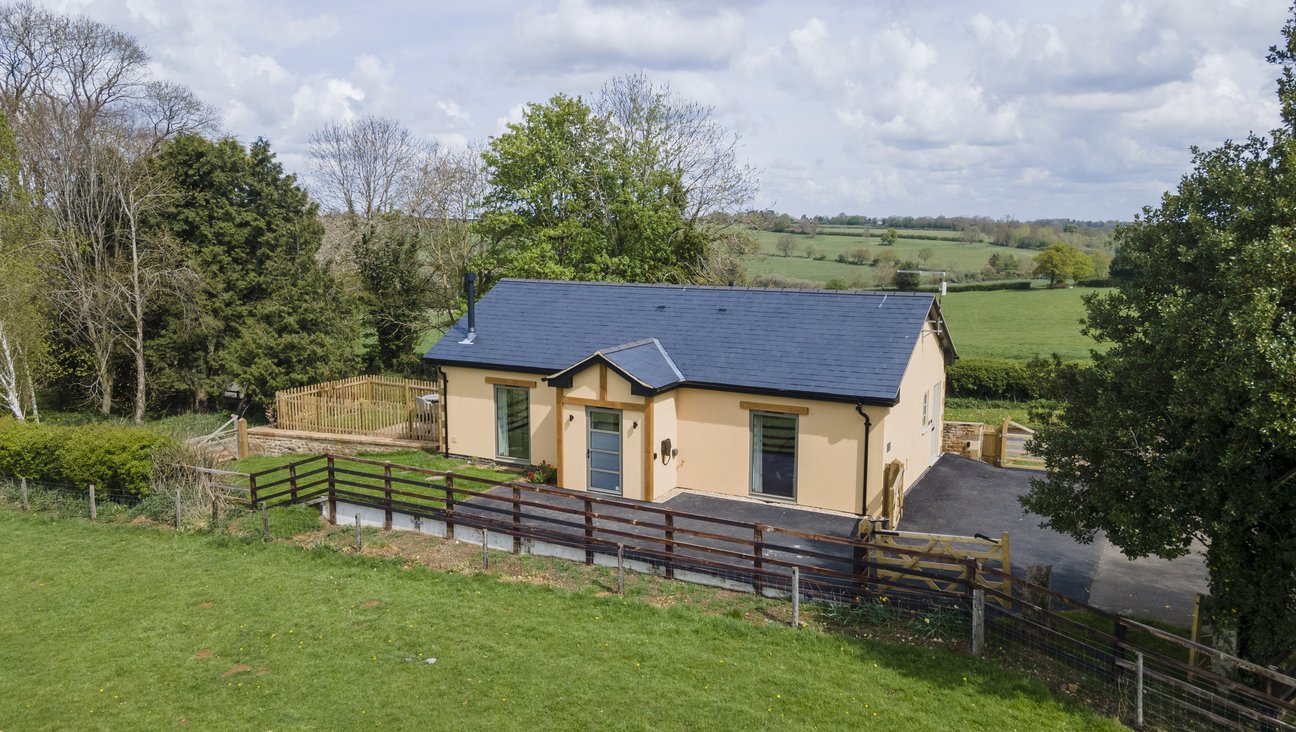 

                                        A craftsman built ionstone bungalow with double patio doors. the left side had floor to ceiling windows and porch rendered in a warm gold with grass, a wall and a picket fence in the foreground
