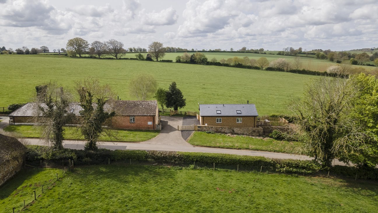 

                                        A tree lined quiet rural road with wide grass verges, smothered in white flowes,  in the village of Ayston Rutland