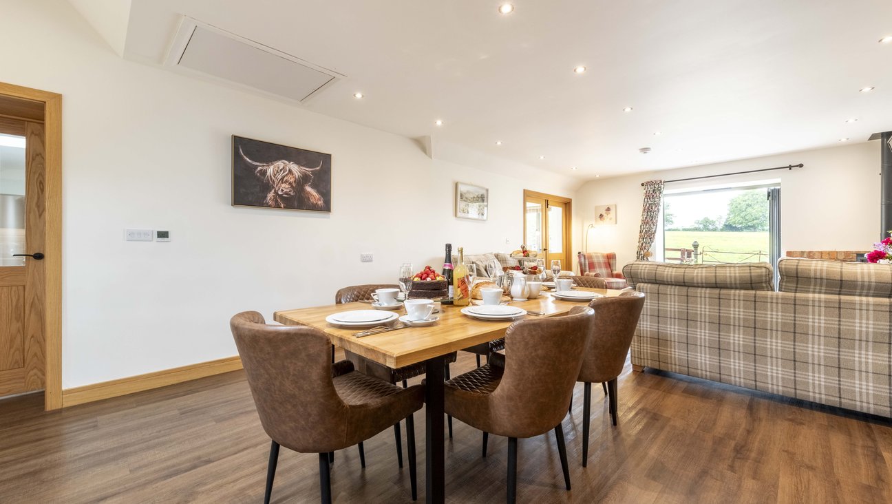 

                                        handmade oak table with leather quilted chairs adjacent to kitchen. table laid with white china, bottles and food.