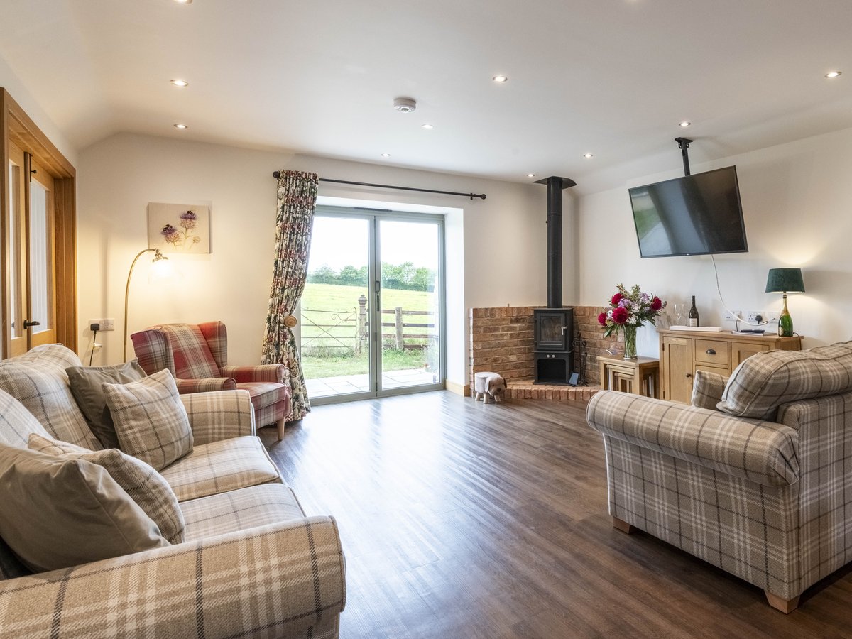Tartan Chair on the left of a patio window, with a brick fireplace and logburner to the right. the view out of the window is out on to parkland with old wrought iron gate in the foreground