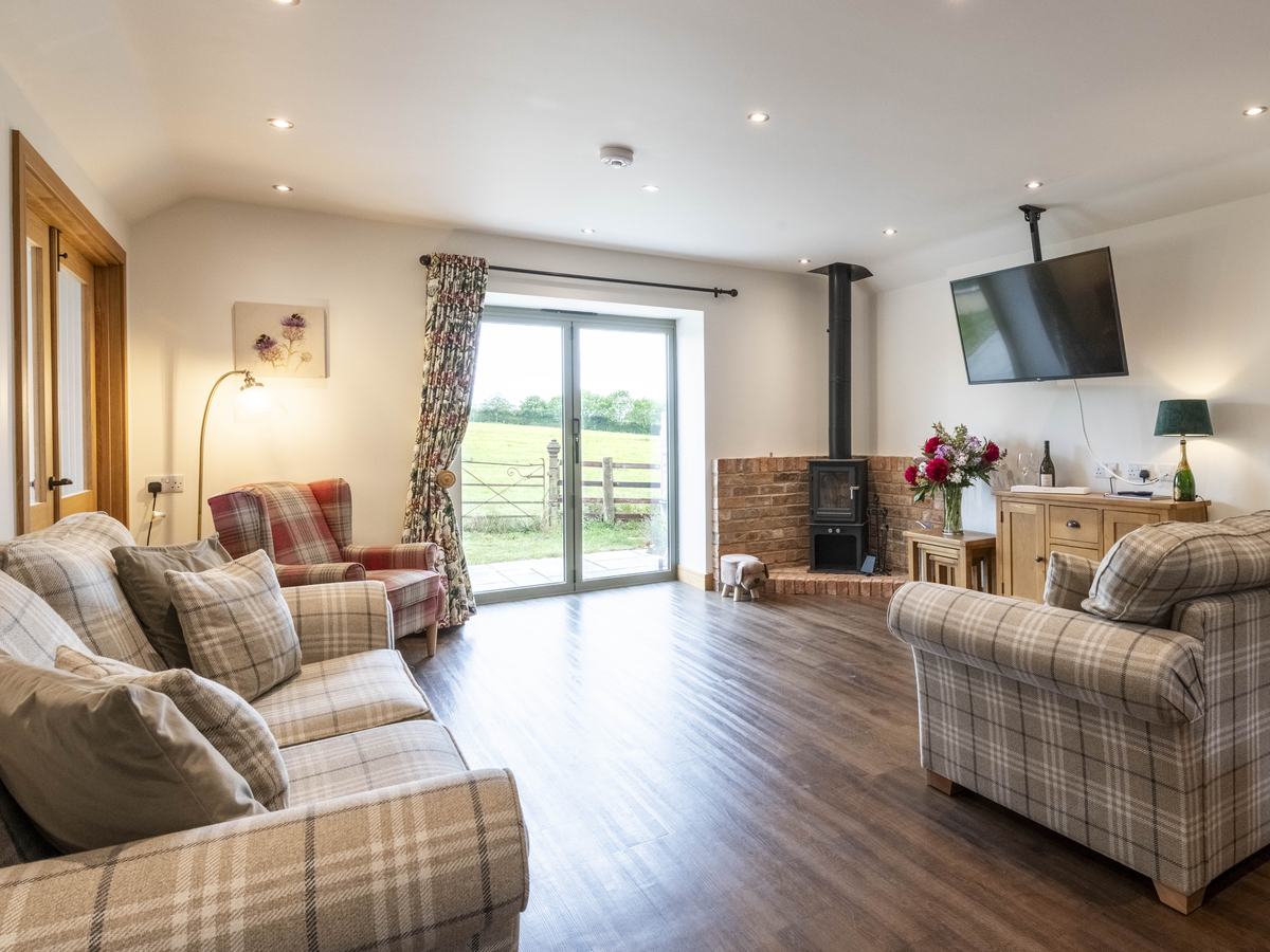 Tartan Chair on the left of a patio window, with a brick fireplace and logburner to the right. the view out of the window is out on to parkland with old wrought iron gate in the foreground