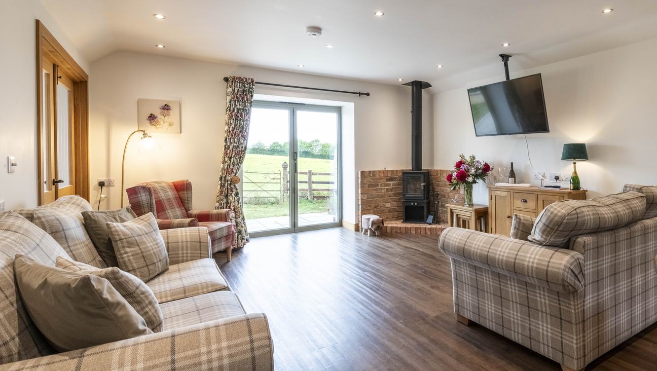 

                                        Tartan Chair on the left of a patio window, with a brick fireplace and logburner to the right. the view out of the window is out on to parkland with old wrought iron gate in the foreground