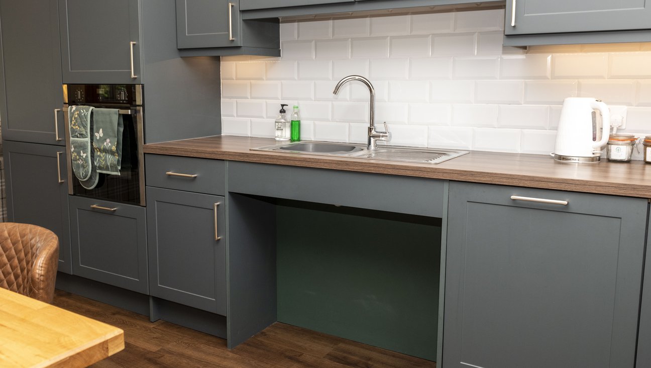 

                                        green kitchen units top and bottom of image, roll under sink in centre with mixer tap and shallow insulated sink, white kettle and toaster.
