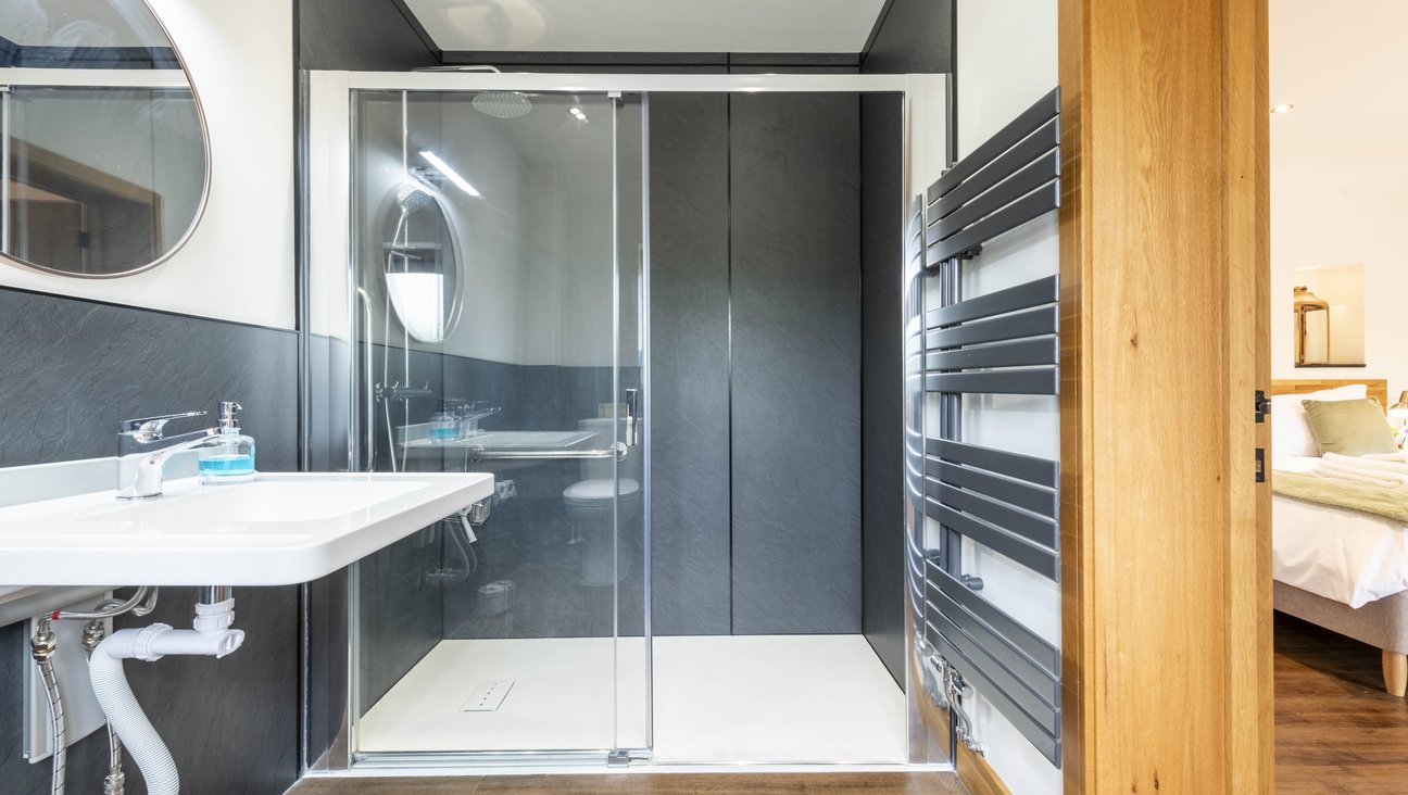 

                                        White adjustable sink with integrated grab rails, a round mirror and shower with level access