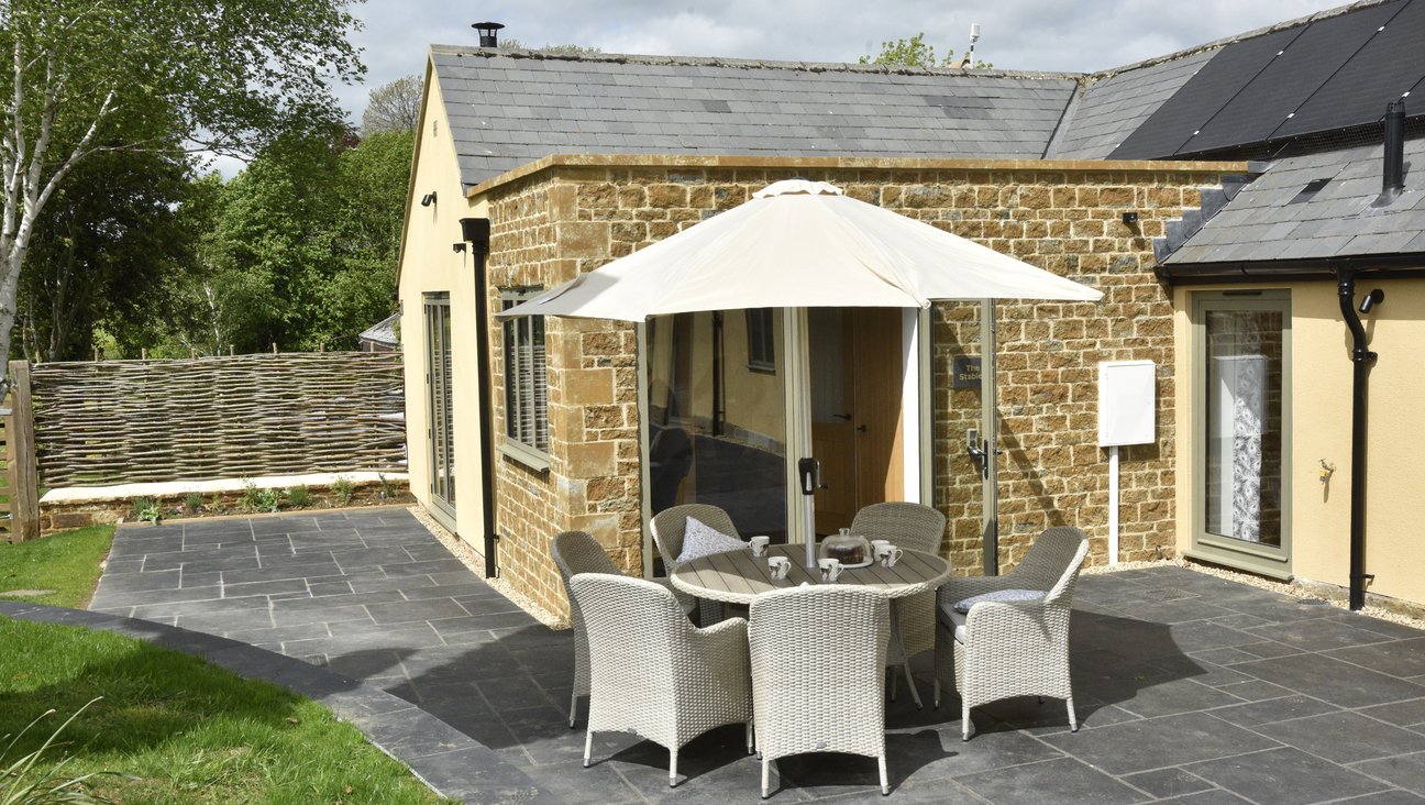

                                        rutland countryside in background, slate patio in foreground, level threshold front door of barn conversion in middle, a round table sits on the patio with a sun umbrella & 6 chairs.