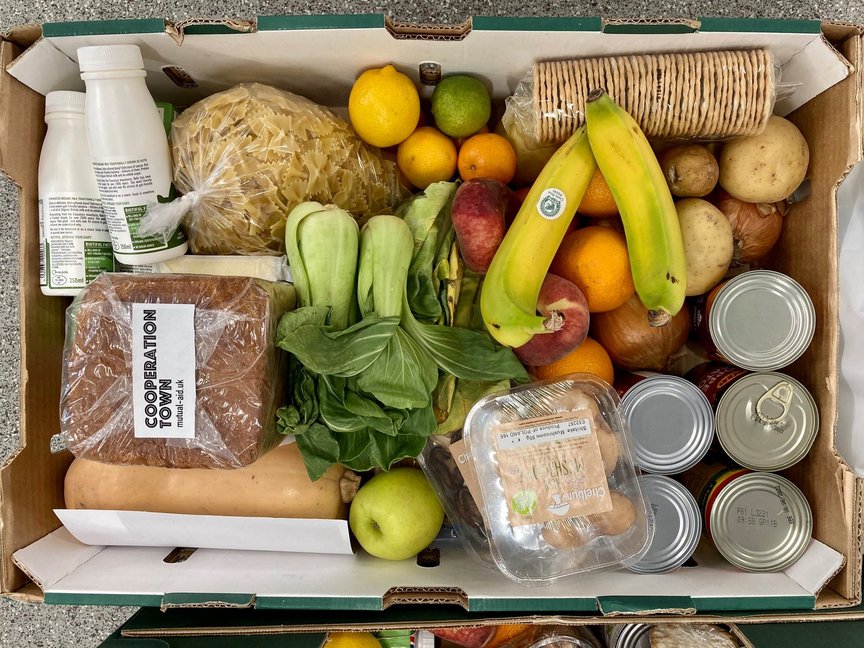 A box of food including lots of fresh fruit and vegetables, bread and cans.