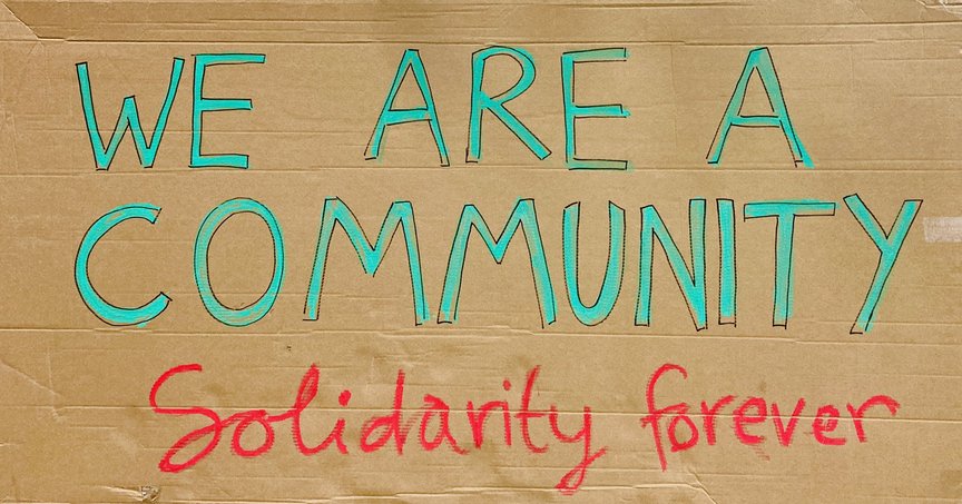 A hand-painted cardboard sign saying "We are a community, solidarity forever."